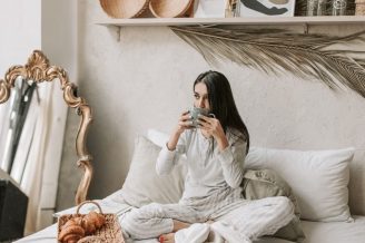 Woman in pajamas enjoys coffee and pastries in a stylish and cozy bedroom setting.